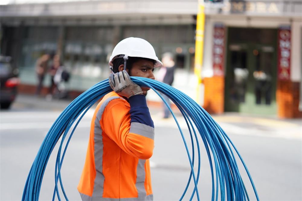 Construction worker carrying blue communications cable on a city street